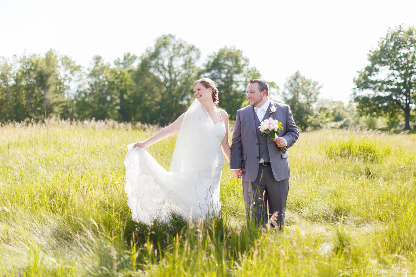 A wedding couple in Ottawa stand in a sunny field looking happy