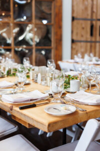 A wooden table is set with plants and elegant glassware in a rustic wedding setting