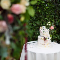 A table stands with a wedding cake and pastels coloured flowers all around it.