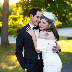 A couple embrace on their wedding day in Ottawa, the bride wears a 1950s style hat and short veil with a sleeveless dress.