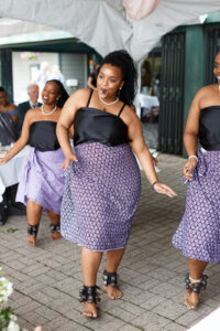 A bridal party dances as a wedding in matching black shirts and patterned blue skirts