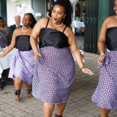 A bridal party dances as a wedding in matching black shirts and patterned blue skirts