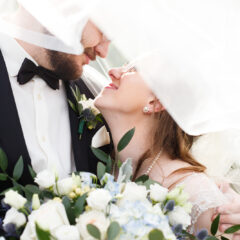a couple is veiled by white on their wedding day with a white bouquet of flowers in the forefront