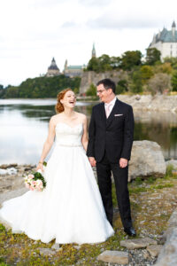 A country Ottawa wedding featuring a happy bride who is a redhead holding a white bouquet and a lake in the background