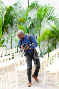 A wedding photographer stands among rows of white chairs before the weddind holding his camera