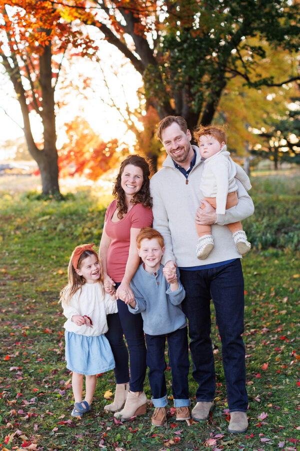 Family of five standing under tree at sunset wearing blue and grey