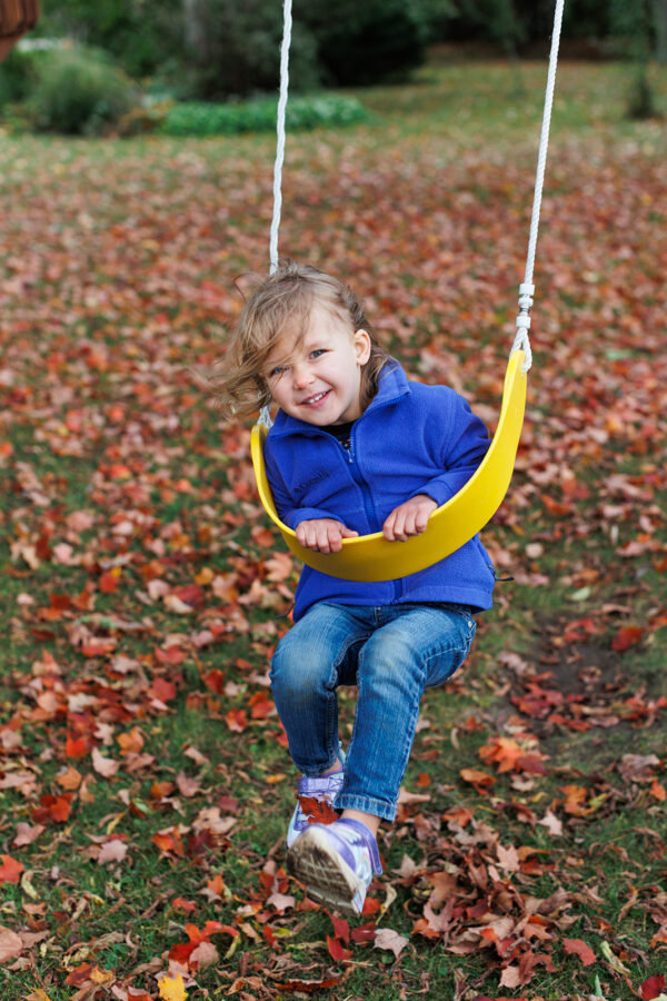 Little girl playing on a swing amid autumn leaves