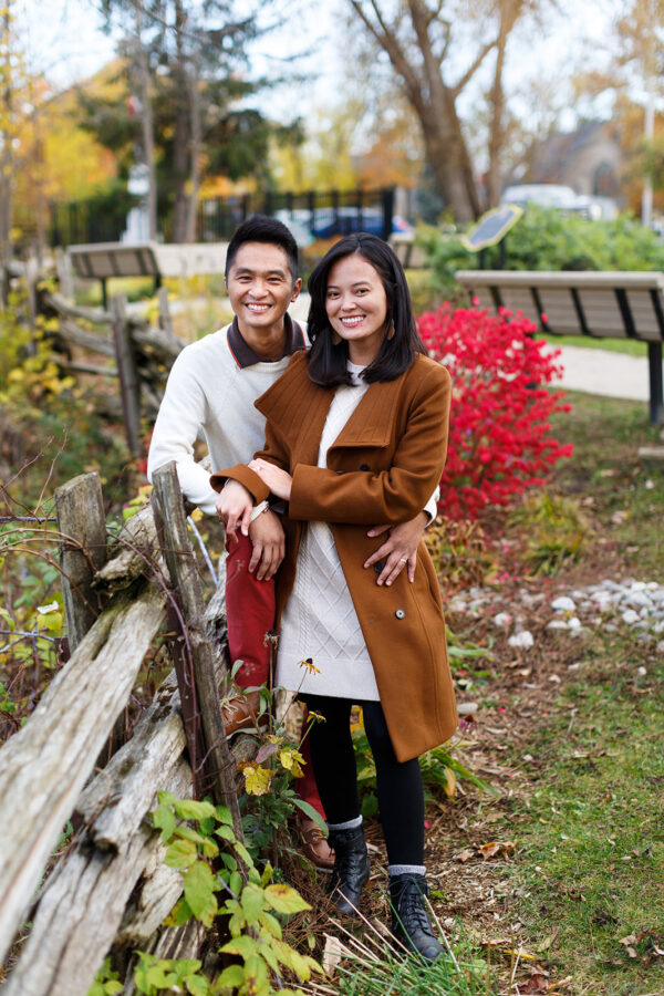 Husband and wife posing against wooden fence in fall