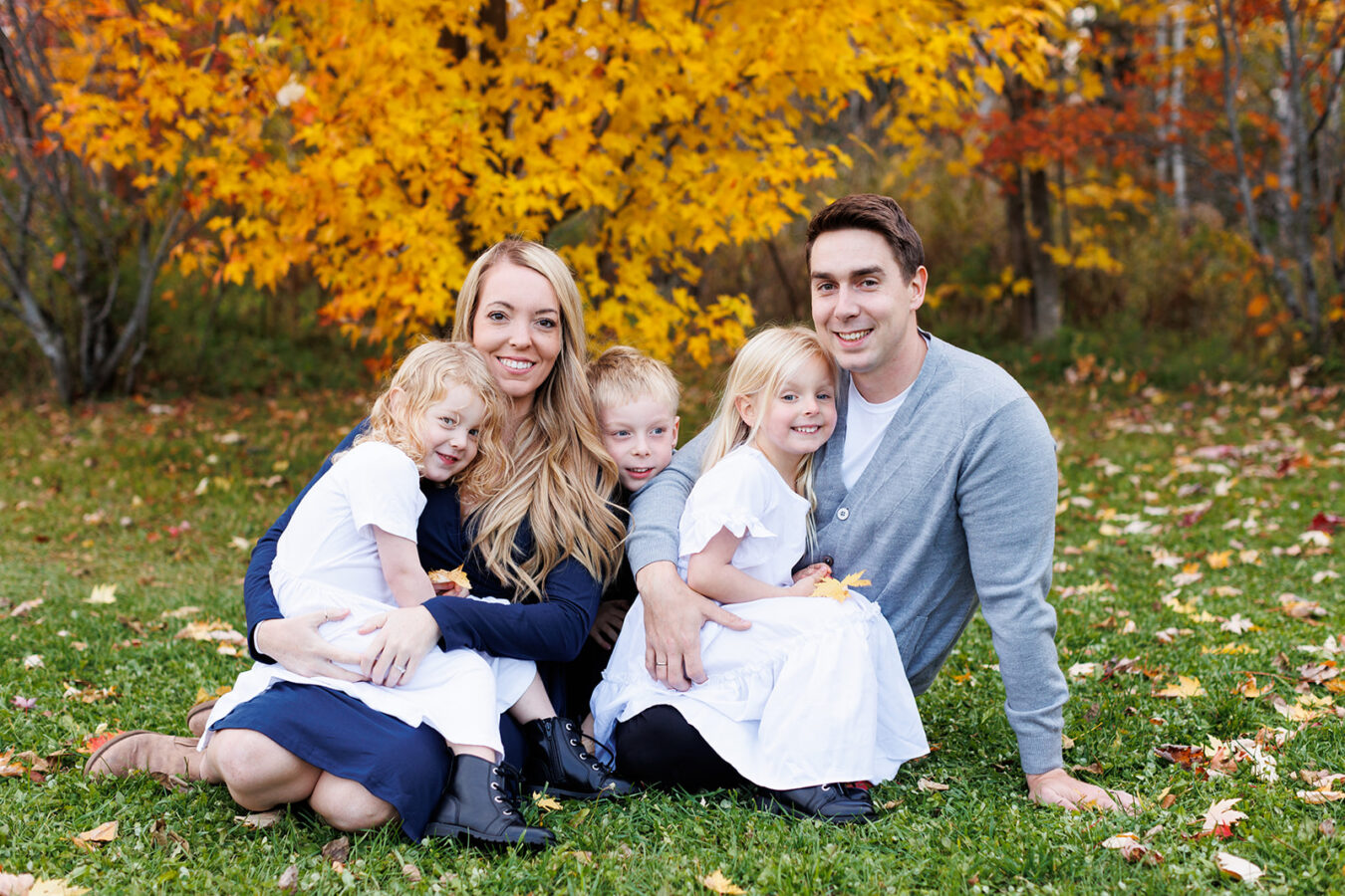 Family of five on grass under yellow tree in fall